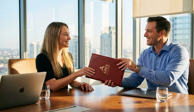 Nhân viên kinh doanh trao bìa kẹp tài liệu cho khách hàng.