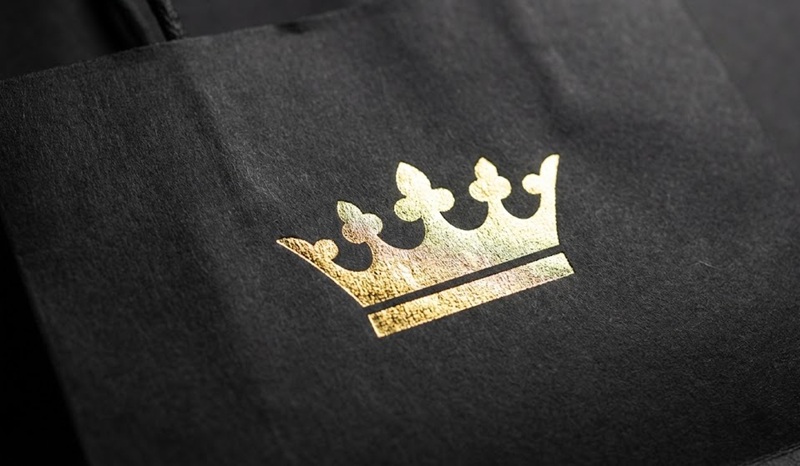 Cận cảnh logo dập nổi ép kim vàng trên nền túi giấy đen nhám.