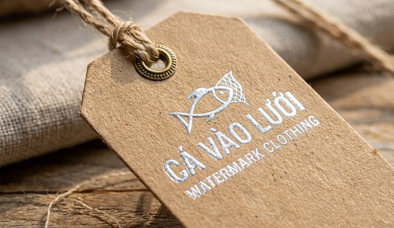 Cận cảnh in thẻ tag treo sản phẩm bằng giấy kraft ép kim bạc.
